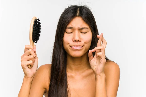 Young Chinese Woman Holding Hairbrush Isolated Crossing Fingers Having Luck — Stockfoto