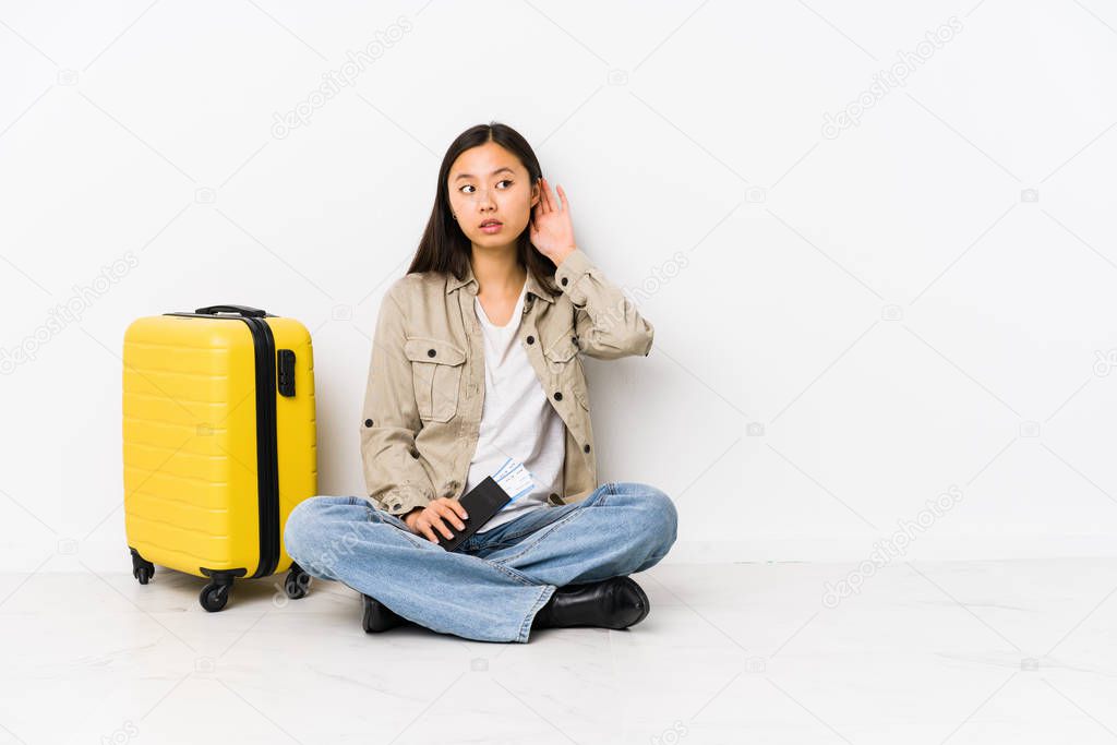 Young chinese traveler woman sitting holding a boarding passes trying to listening a gossip.