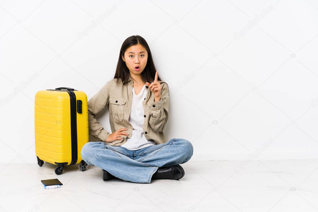 Young chinese traveler woman sitting holding a boarding passes having an idea, inspiration concept.