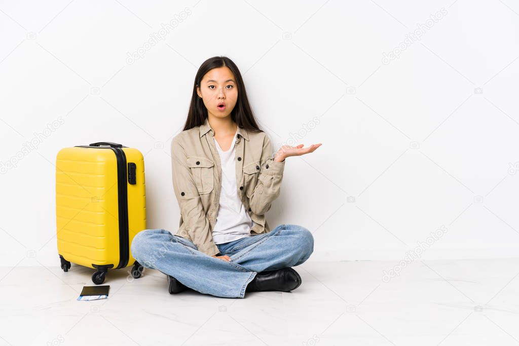 Young chinese traveler woman sitting holding a boarding passes impressed holding copy space on palm.