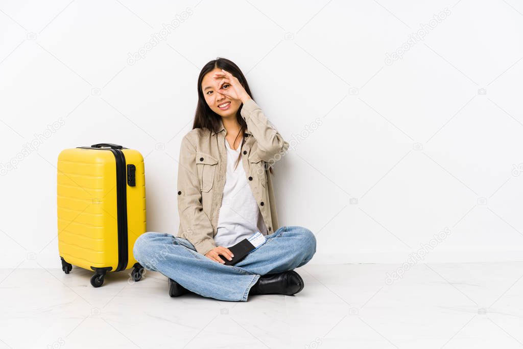 Young chinese traveler woman sitting holding a boarding passes excited keeping ok gesture on eye.