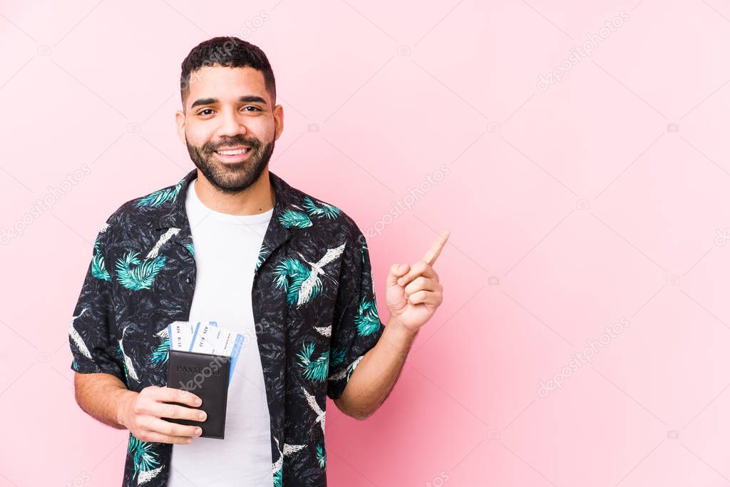 Young arabian cool man holding a boarding passes isolated smiling and pointing aside, showing something at blank space.