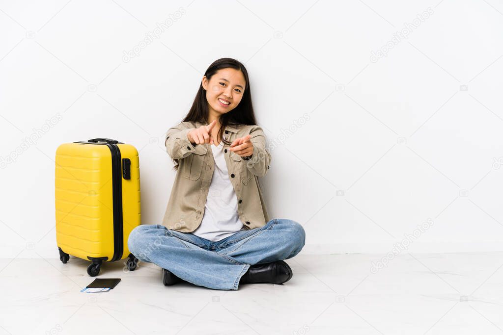 Young chinese traveler woman sitting holding a boarding passes cheerful smiles pointing to front.