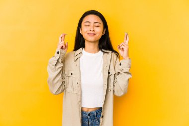 Sarı arka planda izole edilmiş genç Çinli kadın şans getirsin diye dua ediyor.