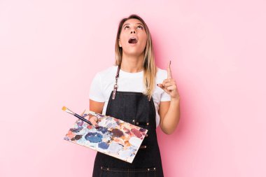 Young artist caucasian woman holding a palett isolated pointing upside with opened mouth.