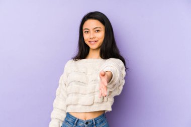 Mor bir arka planda izole edilmiş genç Çinli kadın selamlaşma jesti olarak kameraya elini uzatıyor..