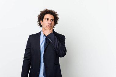 Genç iş adamı beyaz arka plana karşı şüpheli ve şüpheci bir ifadeyle yan bakıyor..