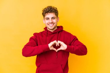  Gülümsüyor ve elleriyle kalp şeklini gösteriyor..