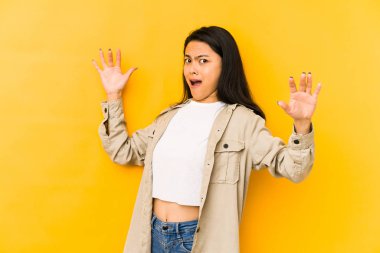 Genç Çinli bir kadın sarı arka planda izole edilmiş. Yakın bir tehlike nedeniyle şoka uğruyor.