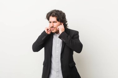 Genç bir iş adamı beyaz arka planda kulakları elleriyle kapatıyor..