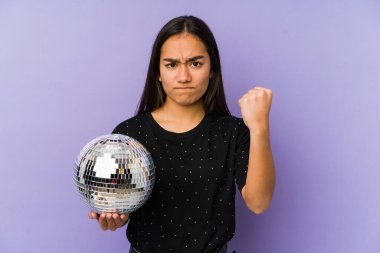 Young asian woman holding a ball party isolated showing fist to camera, aggressive facial expression.