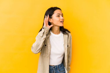Sarı arka planda izole edilmiş genç Çinli kadın bir dedikoduyu dinlemeye çalışıyor..
