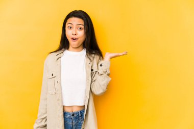 Sarı arka planda izole edilmiş genç Çinli bir kadın avuç içinin fotokopi alanından etkilenmiş..