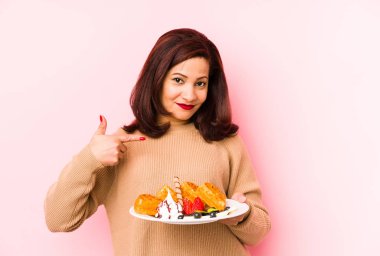 Orta yaşlı Latin bir kadın, elinde waffle tutan, izole edilmiş, gömlek fotokopisini çeken, gururlu ve kendinden emin bir kadın.