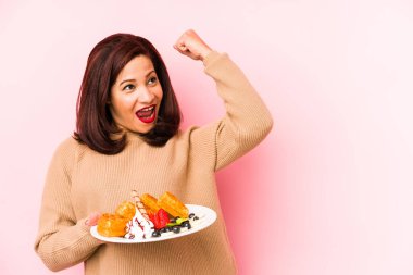 Orta yaşlı Latin kadın waffle 'ı tek başına tutuyor zafer kazandıktan sonra yumruğunu kaldırıyor, kazanan konsept.