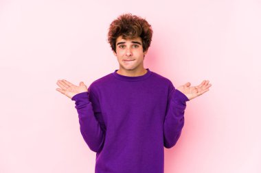 Young caucasian man against a pink background isolated confused and doubtful shrugging shoulders to hold a copy space.