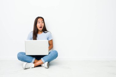 Young mixed race indian woman sitting working on laptop being shocked because of something she has seen.