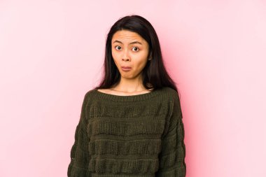 Young chinese woman isolated on a pink background shrugs shoulders and open eyes confused.