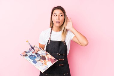 Young artist caucasian woman holding a palett isolated trying to listening a gossip.