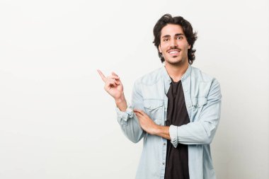 Beyaz arka planda genç yakışıklı adam işaret parmağıyla işaret ederek gülümsüyor..