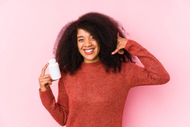 Young afro woman holding a vitamins isolated Young afro woman holding a vitaminsshowing a mobile phone call gesture with fingers.