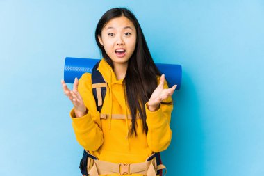 Young chinese backpacker woman isolated receiving a pleasant surprise, excited and raising hands.