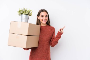 Young caucasic woman holding boxes isolated smiling and pointing aside, showing something at blank space.