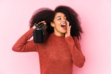 Young afro woman holding a cassete isolated shouting and holding palm near opened mouth.