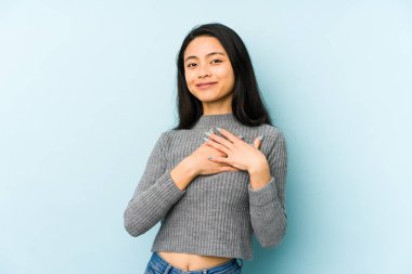 Young chinese woman isolated on a blue background has friendly expression, pressing palm to chest. Love concept.