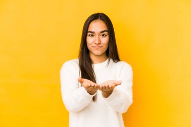 Sarı arka planda izole edilmiş genç bir kadın elinde avuç içi bir şeyle kameraya sunuyor..