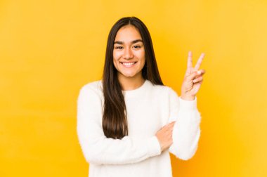 Sarı arka planda izole edilmiş genç bir kadın iki numarayı parmaklarıyla gösteriyor..