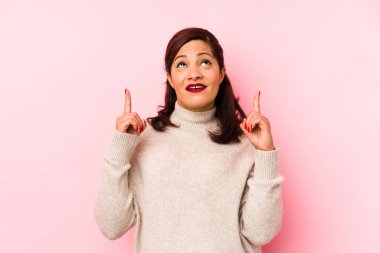 Orta yaşlı, pembe arka planda izole edilmiş, ağzı açık, üst tarafı gösteren Latin bir kadın..