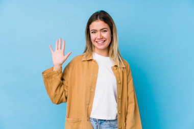Genç beyaz kadın gülümseyerek beş numarayı parmaklarıyla gösteriyor..