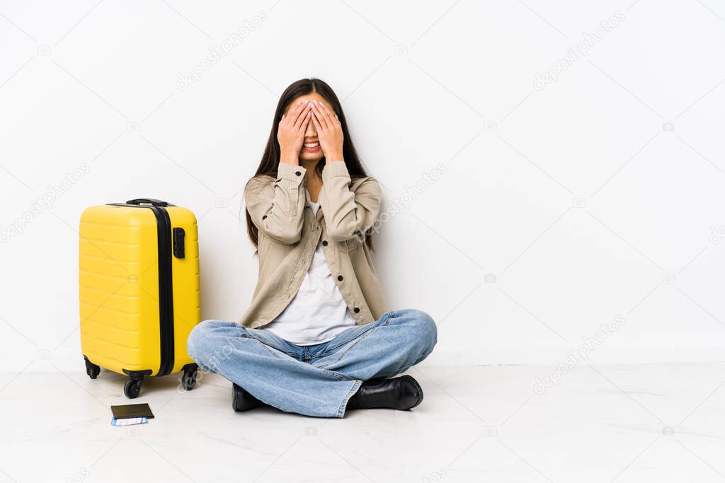 Young chinese traveler woman sitting holding a boarding passes covers eyes with hands, smiles broadly waiting for a surprise.