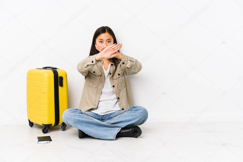 Young chinese traveler woman sitting holding a boarding passes doing a denial gesture