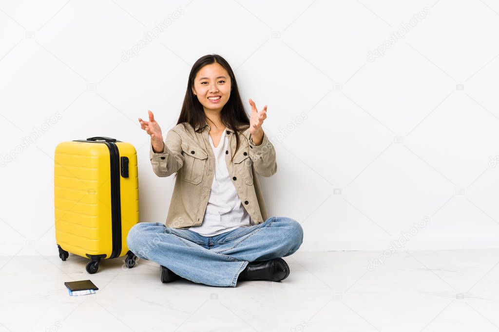 Young chinese traveler woman sitting holding a boarding passes feels confident giving a hug to the camera.