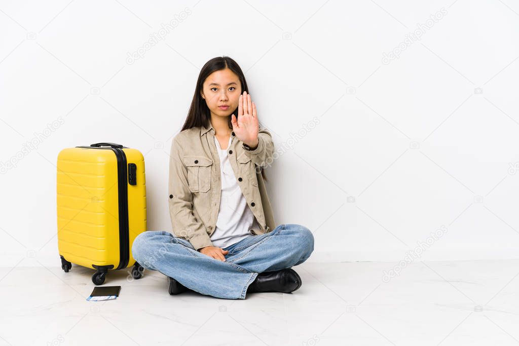 Young chinese traveler woman sitting holding a boarding passes standing with outstretched hand showing stop sign, preventing you.