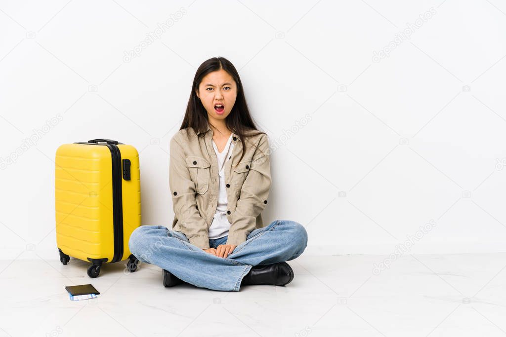 Young chinese traveler woman sitting holding a boarding passes screaming very angry and aggressive.