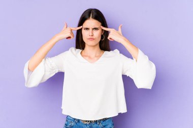 Mor arka planda izole edilmiş genç beyaz kadın bir göreve odaklanmış, parmaklarını işaret ediyor..