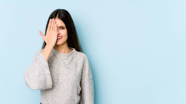 Mavi arka planda izole edilmiş genç beyaz kadın yüzünün yarısını palmiyeyle kaplarken eğleniyor..