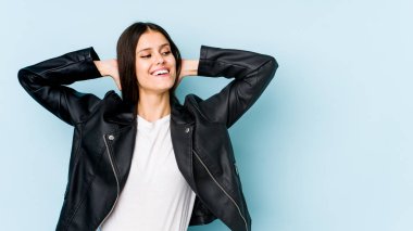 Kafkasyalı genç bir kadın mavi arka planda izole edilmiş, kendinden emin, elleri başının arkasında..