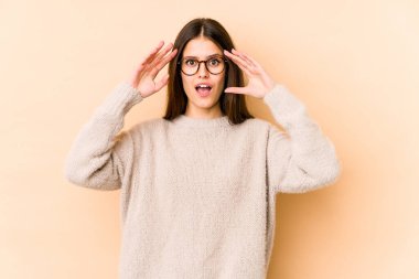 Beyaz tenli genç bir kadın bej arka planda izole edilmiş. Hoş bir sürprizle karşılaşıyor. Heyecanlı ve el kaldırıyor..