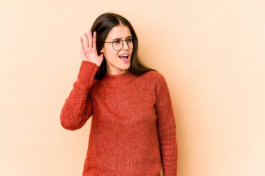 Beyazlı genç bir kadın bej arka planda izole edilmiş bir şekilde bir dedikoduyu dinlemeye çalışıyor..