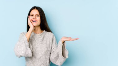 Mavi arka planda izole edilmiş beyaz bir kadın avuç içinde fotokopi alanı tutuyor, el üstünde tutuyor. Şaşırmış ve mutlu..
