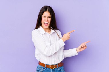 Mor arka planda izole edilmiş genç beyaz kadın işaret parmaklarıyla fotokopi alanını işaret ederek heyecan ve arzusunu ifade ediyor..