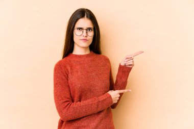 Beyazlı genç bir kadın bej arka planda izole edilmiş. İşaret parmaklarıyla bir fotokopi alanını işaret ederek şok olmuş..