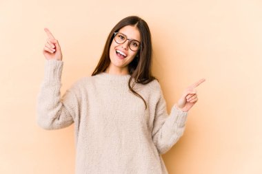 Beyaz tenli genç bir kadın bej arka planda izole edilmiş, farklı kopya alanlarını işaret ediyor, birini seçiyor, parmağıyla gösteriyor..