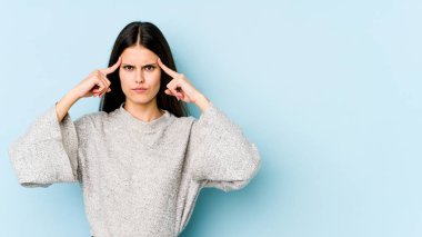 Kafkasyalı genç bir kadın mavi arka planda izole edilmiş bir vazifeye odaklanmış, parmaklarını işaret ediyor..