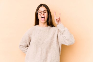 Beyaz tenli genç bir kadın bej arka planda izole edilmiş. Parmaklarıyla taş hareketi gösteriyor.