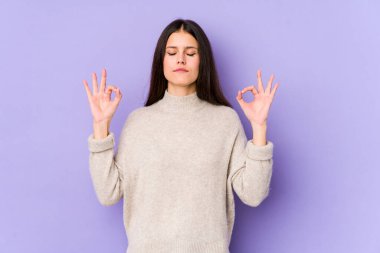 Mor arka planda izole edilmiş genç beyaz kadın yoğun bir günün ardından rahatlıyor, yoga yapıyor..